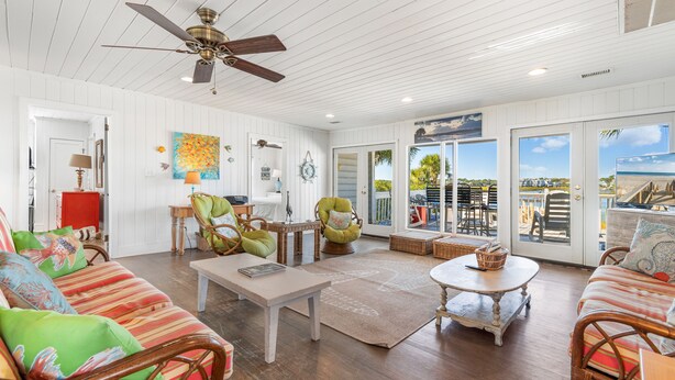 A spacious living room with wooden floors, a ceiling fan, and a large window overlooking a scenic view. - Inlet Front Beach House 4BR 4BA Pet Friendly Private Dock (Garden City Beach)