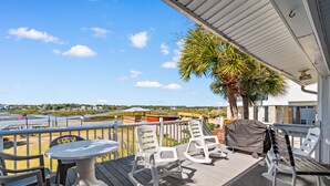 A covered outdoor deck with a table and chairs, overlooking a beach and ocean. - Inlet Front Beach House 4BR 4BA Pet Friendly Private Dock (Garden City Beach)