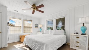 A bedroom with a large bed, white walls, wooden floors, a ceiling fan, and a window with blinds. - Inlet Front Beach House 4BR 4BA Pet Friendly Private Dock (Garden City Beach)