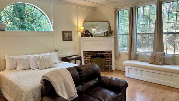 Ein Schlafzimmer mit einem Bett, einer Ledersofa, einem Kamin und großen Fenstern mit Vorhängen.