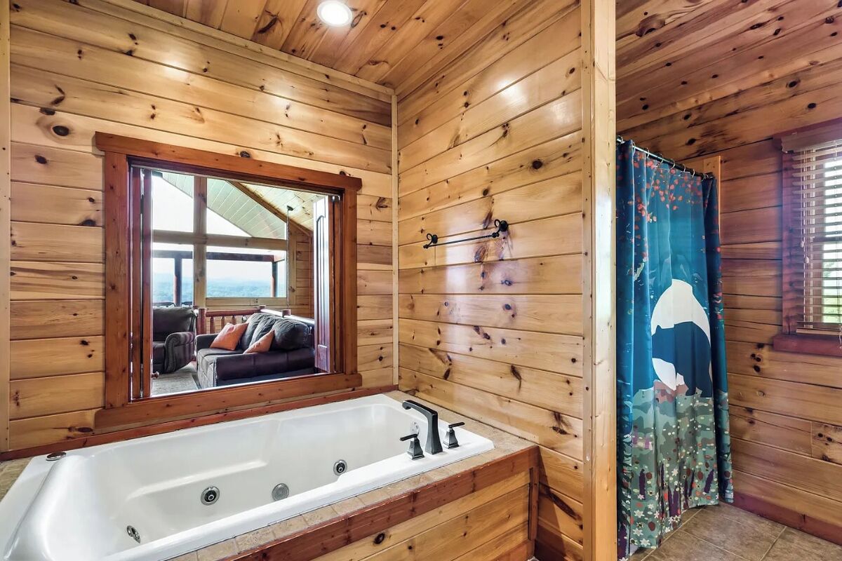 Een houten badkamer in een vakantiehuisje, met een groot bad, een spiegel en een douchegordijn.
