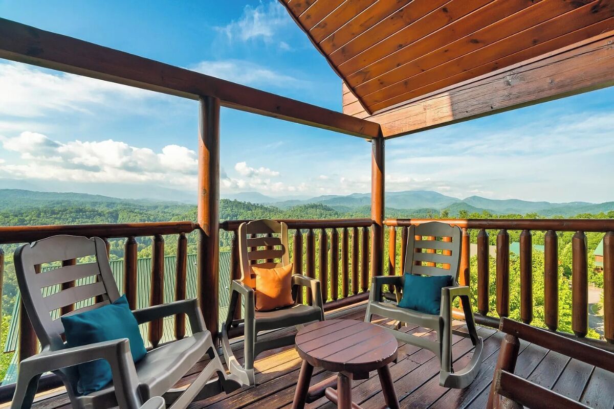 Una terraza de madera con dos mecedoras y una pequeña mesa, con vistas a un paisaje montañoso.