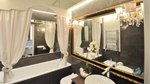 A modern bathroom with a large mirror, white curtains, a bathtub, a sink, and a chandelier.