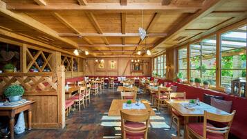 Ein geräumiges Restaurant mit Holzvertäfelungen, mehreren Sitzbereichen und großen Fenstern, die viel Tageslicht hereinlassen.
