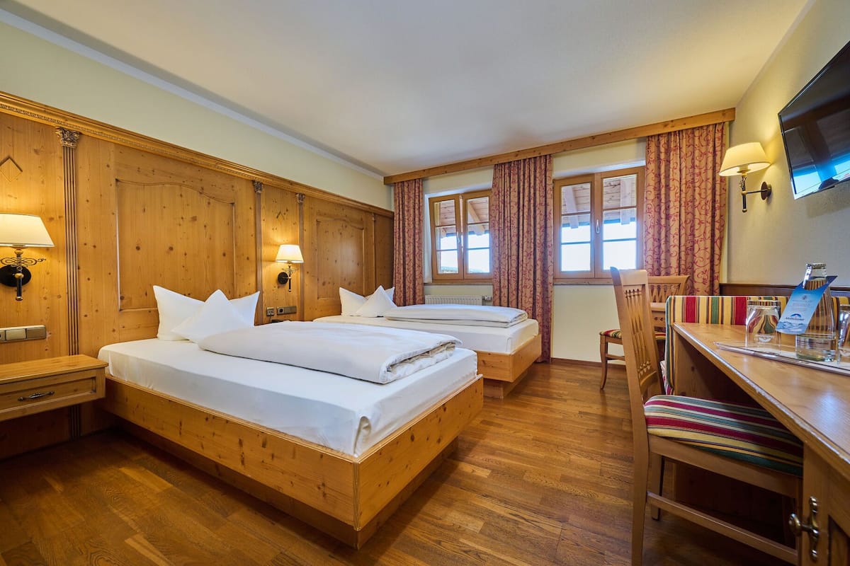 Une chambre d’hôtel avec deux lits en bois, un bureau avec une chaise, une télévision et une fenêtre avec des rideaux.