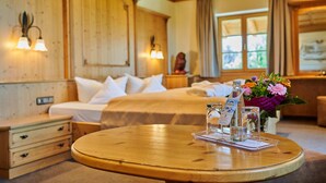 Une chambre d’hôtel avec un intérieur en bois, un lit avec du linge de maison blanc, une table ronde en bois sur laquelle est posé un menu, et un vase rempli de fleurs.