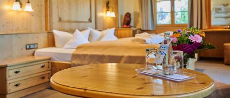 Ein Hotelzimmer mit Holzvertäfelung, einem Bett mit weißen Leinen, einem runden Holztisch mit einer Speisekarte und einer Vase mit Blumen.