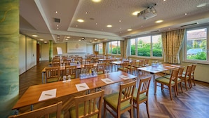 Une grande salle de conférence équipée de plusieurs tables et chaises, d’un projecteur et d’une enseigne sur laquelle on peut lire « HAPPENER ».