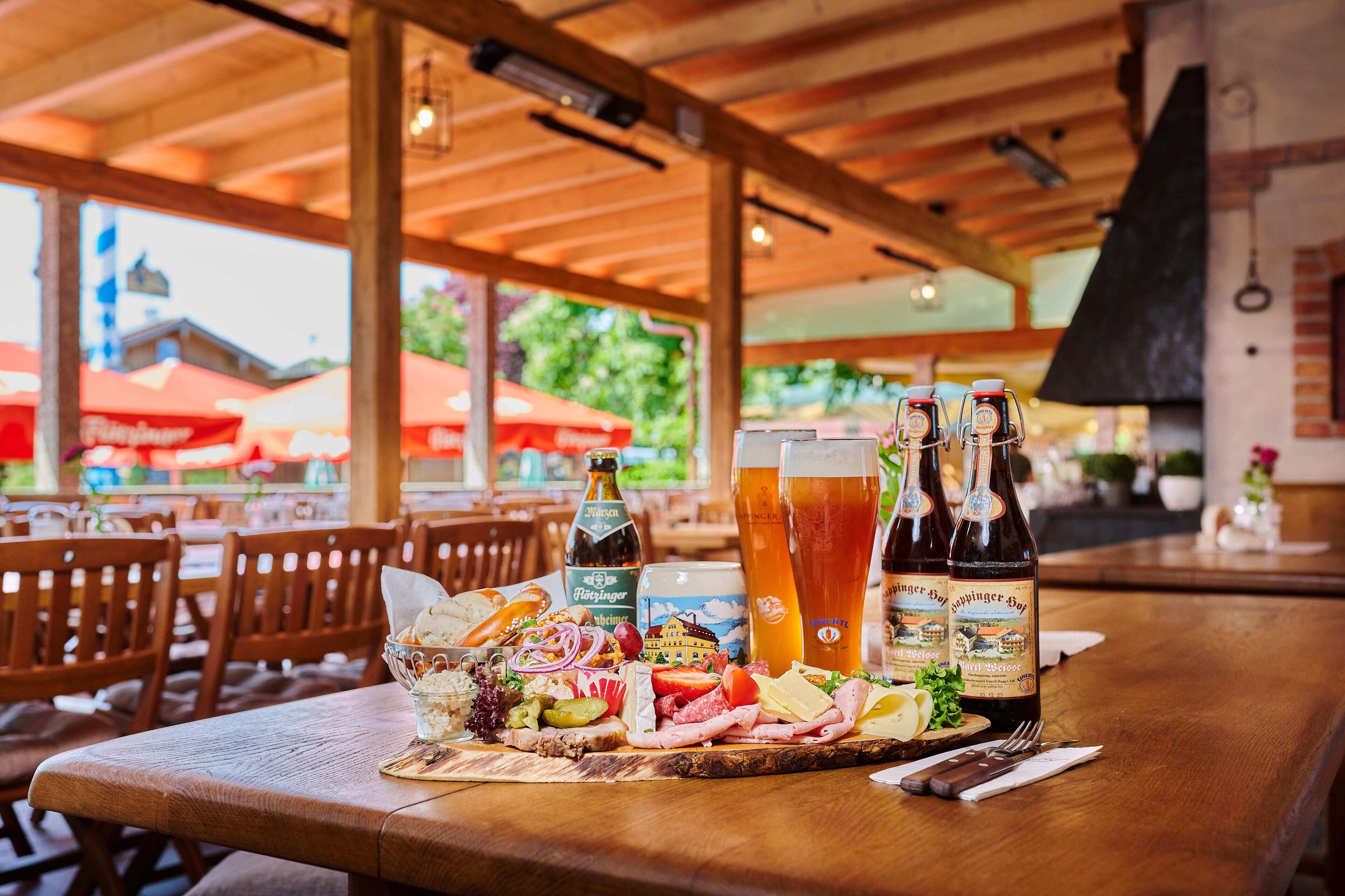Une table en bois avec une planche de charcuterie, des bouteilles de bière et un verre de bière.