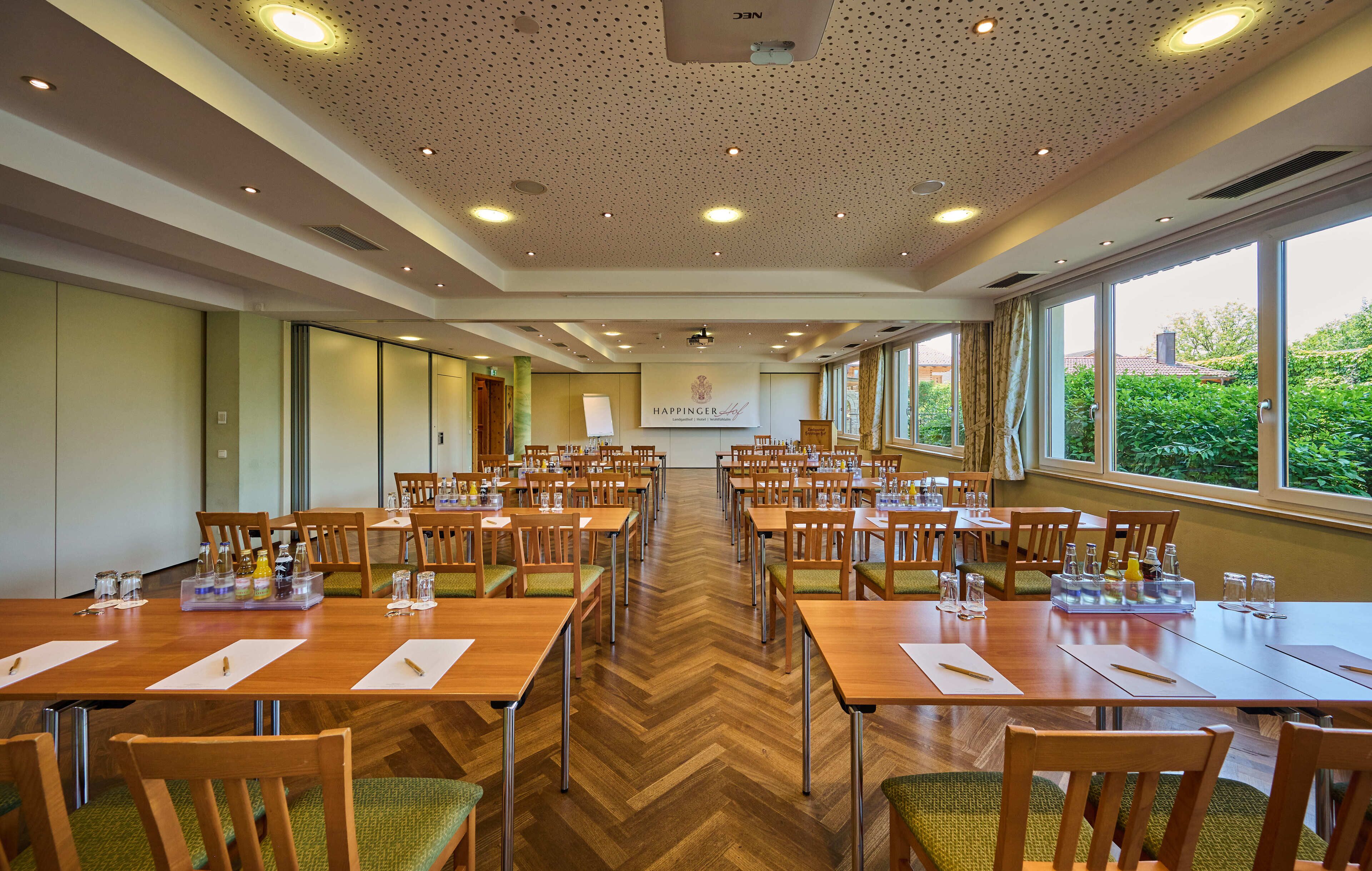 A conference room with multiple tables and chairs, a projector screen, and a banner with the text "HAPPINGER".