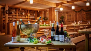 Un intérieur en bois où une table est dressée pour une dégustation de vins, avec des bouteilles, des verres, ainsi qu’une variété de fromages et de fruits.