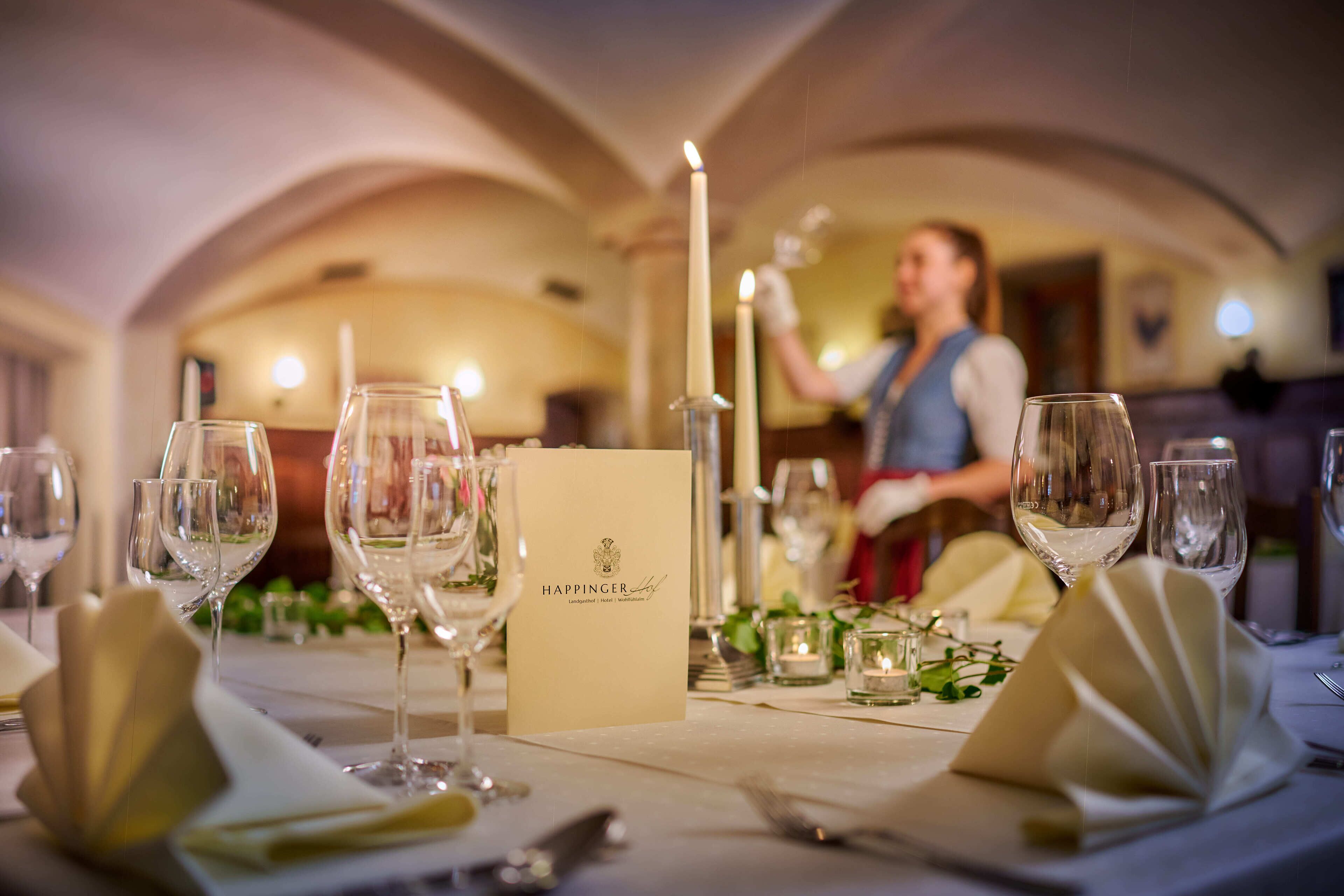 Una mesa de comedor preparada con copas de vino, un menú y velas.