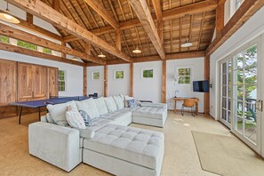 A spacious room with a wooden ceiling, a sectional sofa, a ping pong table, and a television.