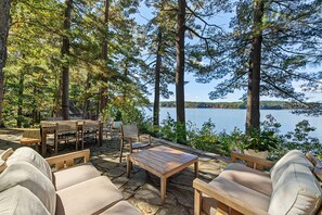 An outdoor seating area with stone flooring, wooden furniture, and a view of a lake.