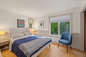 A bedroom with a bed, a chair, a window, and two framed pictures on the wall.