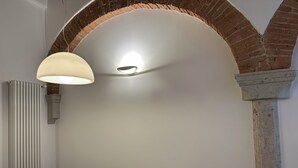 A dining area with a brick arch, a table with chairs, a white plate, and a pendant light. - Il nido dell'Upupa (Montepulciano)