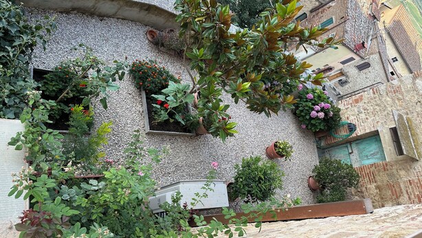 A courtyard with potted plants, a small garden area, and a building with a stone facade. - Il nido dell'Upupa (Montepulciano)