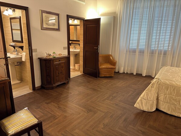 A hotel room with a wooden floor, a sofa, a chair, a cabinet, a sink, and a mirror. - Il nido dell'Upupa (Montepulciano)