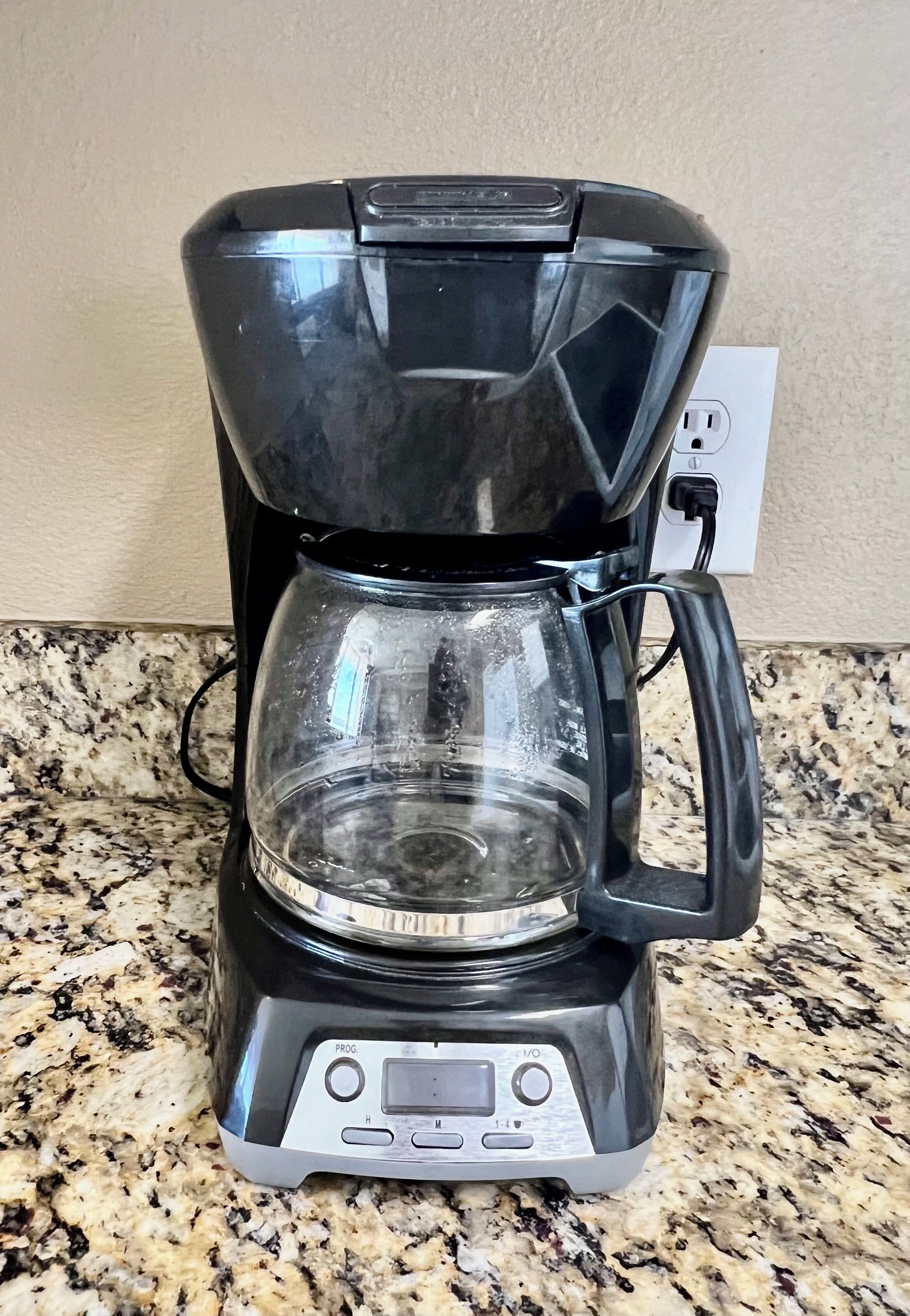 A black coffee maker with a digital display and a transparent water reservoir on a granite countertop.