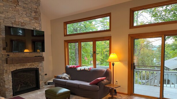 A cozy living room with a stone fireplace, a grey sofa, a small table, and a lamp. - Lake Breeze Hideaway | Lake Winnipesaukee Vacation Home in Patrician Shores (Meredith)