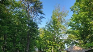 A residential area with a paved driveway, a house with a porch, and a car parked in the driveway. - Lake Breeze Hideaway | Lake Winnipesaukee Vacation Home in Patrician Shores (Meredith)