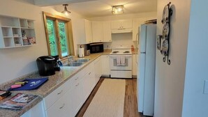 A modern kitchen with white cabinets, a granite countertop, and a built-in microwave. - Lake Breeze Hideaway | Lake Winnipesaukee Vacation Home in Patrician Shores (Meredith)