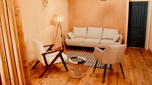 Un salon chaleureux avec un canapé, deux fauteuils, une lampe sur pied et un tabouret en osier.