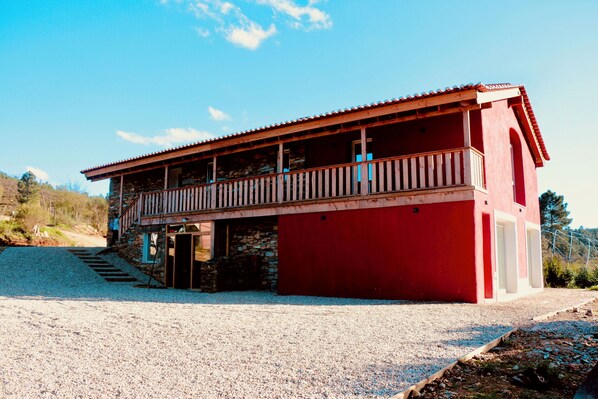Un bâtiment rouge doté d’un balcon, avec une fondation en pierre et une allée gravillonnée.