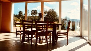 Un espace repas comprenant une table et des chaises, de grandes fenêtres et une vue sur l’extérieur.