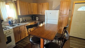 A kitchen with wooden cabinets, a dining table with four chairs, a refrigerator, and a stove. - Poland Hill Hideaway, located in the beautiful woods surrounding Tionesta, PA (Tionesta)