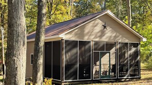 A single-story building with a covered porch, surrounded by trees. - Poland Hill Hideaway, located in the beautiful woods surrounding Tionesta, PA (Tionesta)