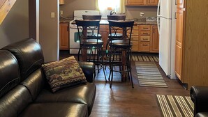 A compact kitchen with wooden cabinets, a refrigerator, and a dining area with two chairs. - Poland Hill Hideaway, located in the beautiful woods surrounding Tionesta, PA (Tionesta)