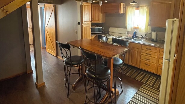 A spacious kitchen with wooden cabinets, a dining table with chairs, and a hanging light fixture. - Poland Hill Hideaway, located in the beautiful woods surrounding Tionesta, PA (Tionesta)