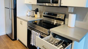 A modern kitchen with stainless steel appliances, including a refrigerator, microwave, and oven. - 7th Floor 1-Bedroom Condo with Parking (Calgary)