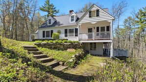 A two-story house with a front porch, a covered porch area, and a stone staircase leading up to the entrance. - Charming Riverview Cottage Home in Black River Falls (Black River Falls)