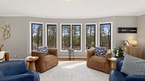 A living room with two sofas, a coffee table, and large windows with a view of trees. - Charming Riverview Cottage Home in Black River Falls (Black River Falls)