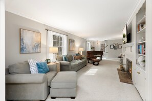 A living room with a sofa, ottoman, and a piano. - Charming Riverview Cottage Home in Black River Falls (Black River Falls)