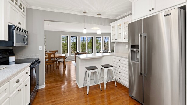 A modern kitchen with white cabinetry, stainless steel appliances, and a wooden floor. - Charming Riverview Cottage Home in Black River Falls (Black River Falls)