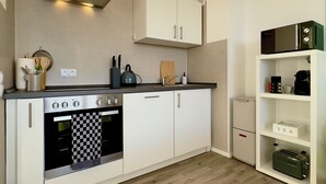 Eine kleine Küche mit weißen Schränken, einem eingebauten Backofen und einer Mikrowelle auf der Arbeitsfläche.