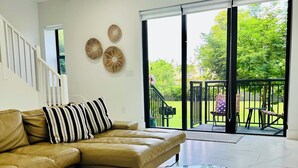 Un salon moderne avec une table basse en verre, un canapé beige et une vue sur un jardin, visible à travers une porte-fenêtre.