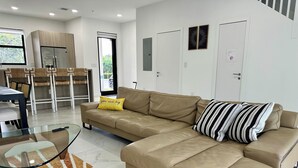 Un salon moderne avec un canapé d’angle beige, une table basse en verre et un tapis à motifs.