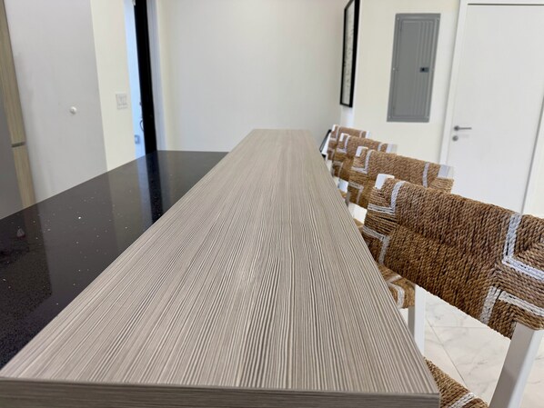 A long, rectangular dining table with a textured surface, surrounded by chairs with woven seats.
