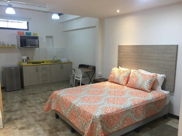 Une chambre avec un lit, un bureau et un coin cuisine.