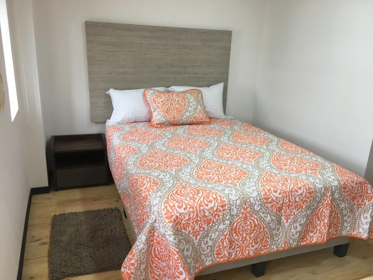 Una cama individual con una colcha estampada, cabecero, mesita de noche y alfombra.