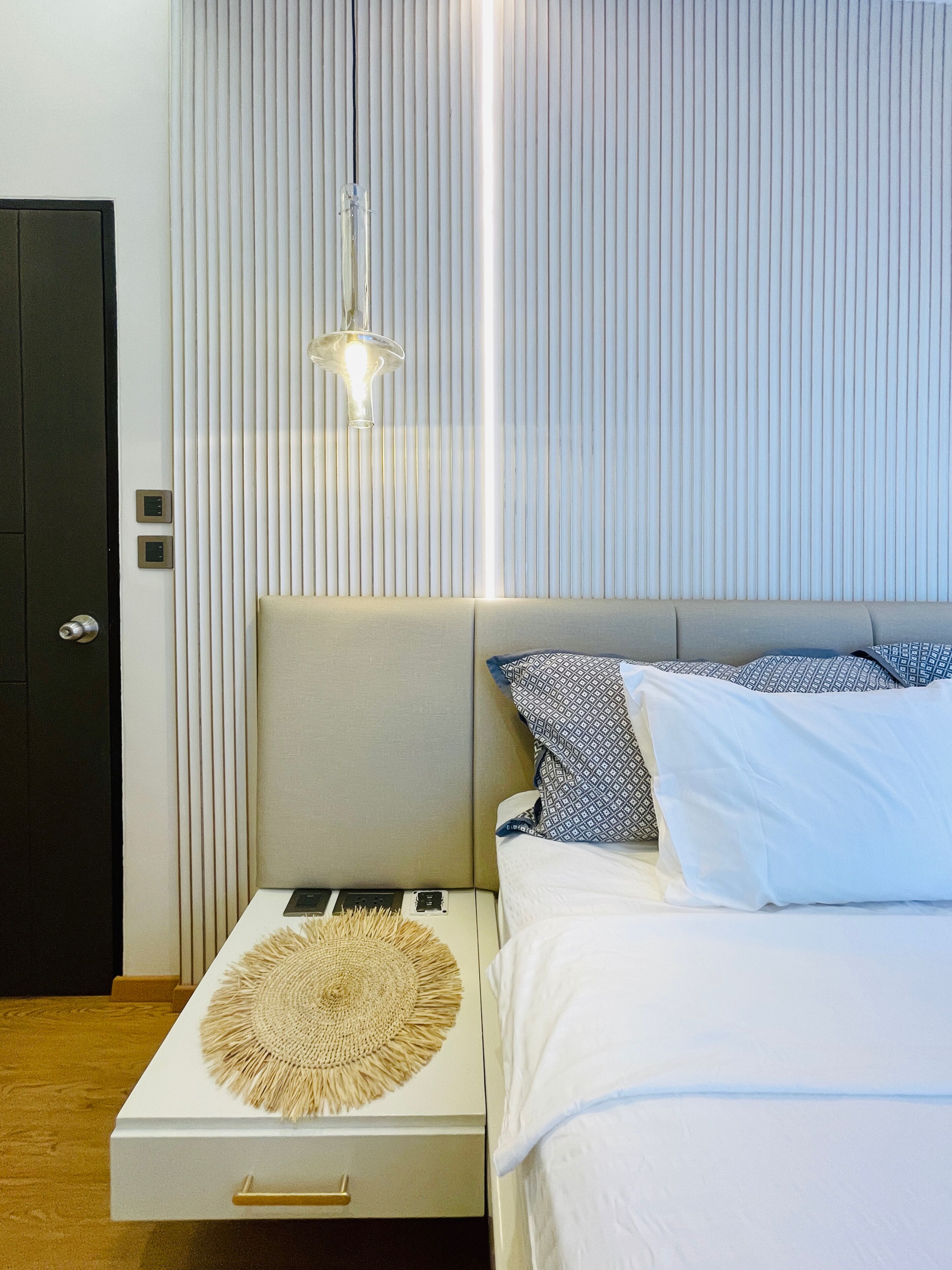 Quarto moderno com cama, mesas de cabeceira, luminária na parede e uma porta.