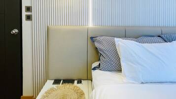 Quarto moderno com cama, mesas de cabeceira, luminária na parede e uma porta.