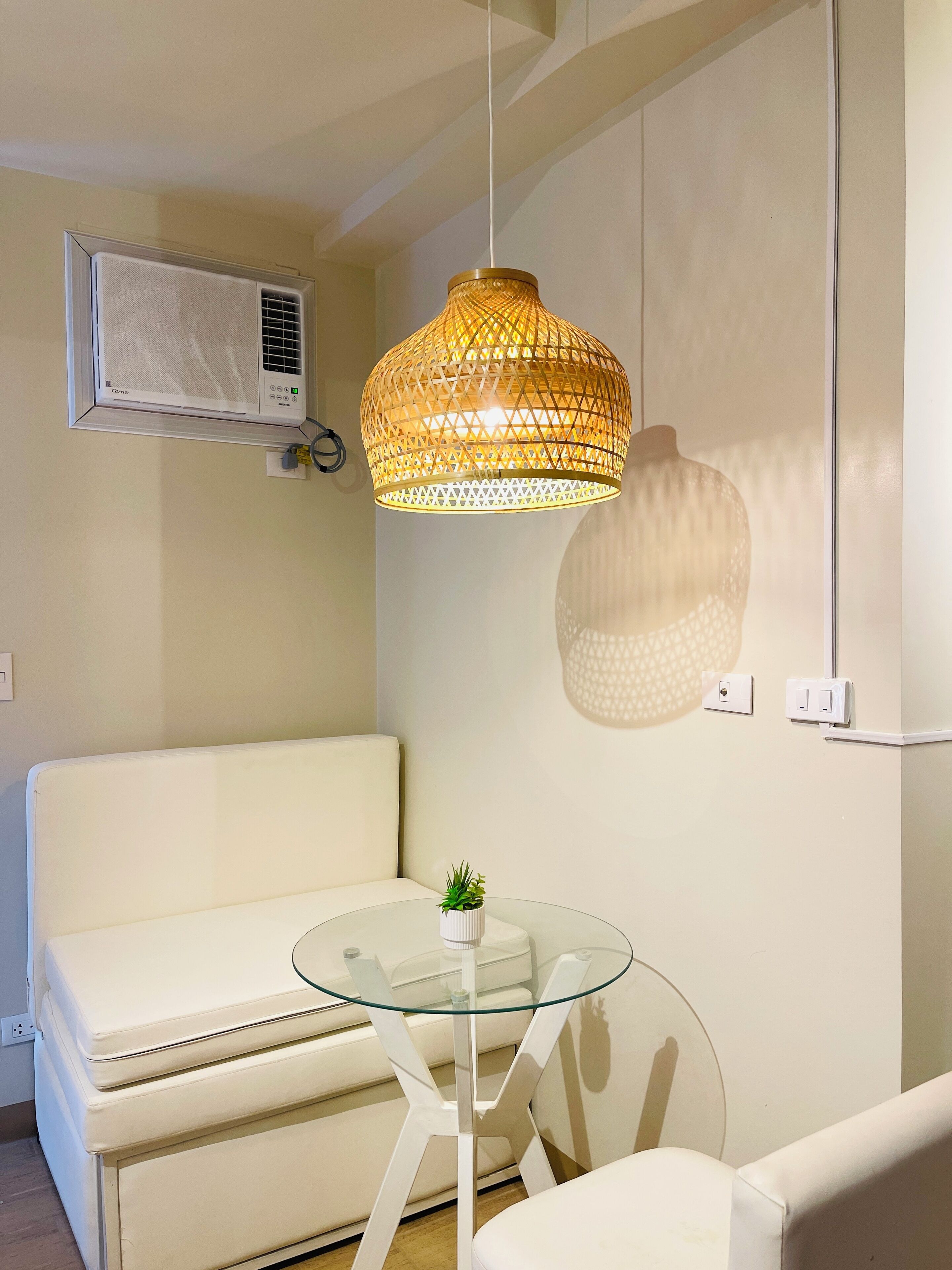 Een moderne woonruimte met een witte bank, een glazen tafel met een klein plantje, en een bijzondere geweven hanglamp.