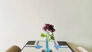 A table with a blue vase containing flowers, set on a patterned tablecloth.