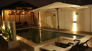 Une piscine extérieure dotée de chaises longues et d’un parasol, entourée d’une clôture en bois et d’un petit escalier.