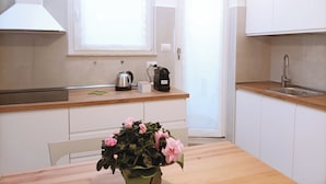 Une cuisine moderne avec des meubles blancs, un plan de travail en bois, une bouilloire, une machine à café et une plante en pot.